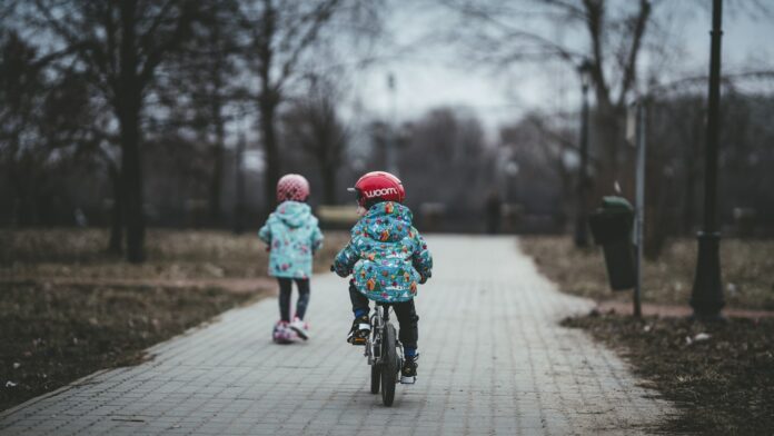 Photo by Arseny Togulev child riding with bike and another child walking on concrete pavement near trees