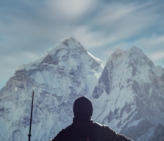 젊게 사는 비법 a man holding a rifle while standing on top of a mountain