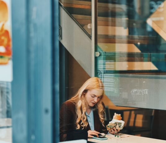 바쁜 일상 속 ‘마음 챙김 식사’ 실천법… 건강한 습관으로 거듭나기 Woman eating a sandwich at a cafe table.