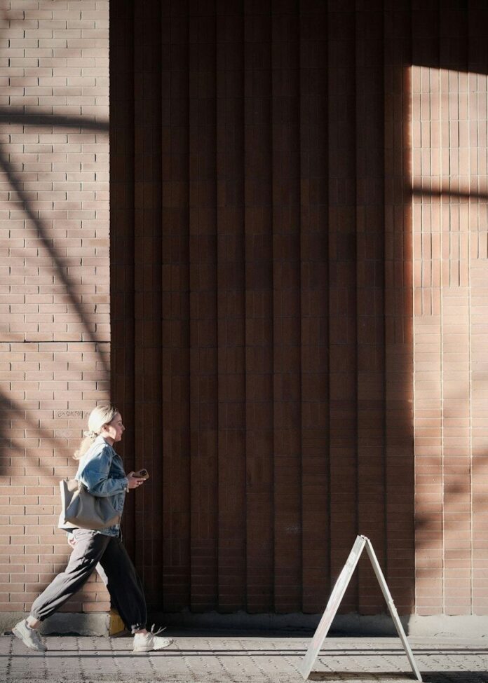 Woman walking past a brick building with shadows
